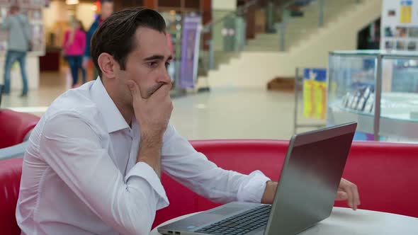 Stressed Businessman Working with His Laptop at Table in Patio of Restaurant