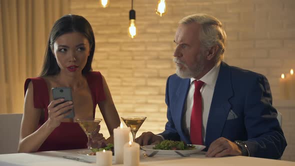 Girl Sitting in Restaurant With Boring Old Man, Chatting on Phone, Bad Date
