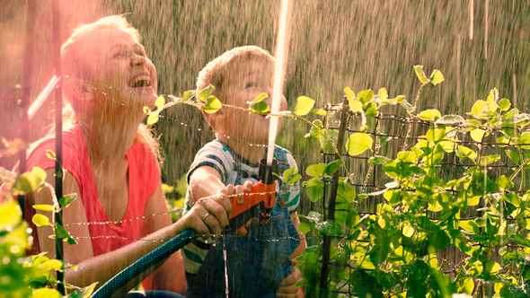 Mother Helping Son To Water The Garden With Hose
