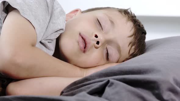 Little preschool boy sleeping in his bed lying on his side. A boy in a gray T-shirt.