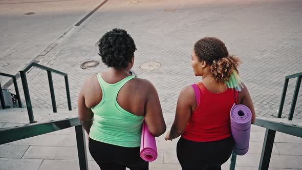 Back View of Positive African American Ladies in Sportswear Going Downstairs with Fitness Mats