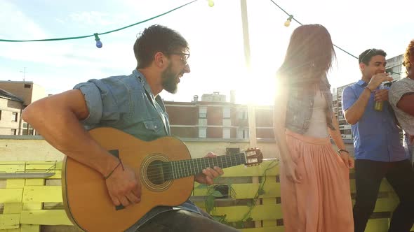 Happy musician playing guitar for a group of people at the rooftop party