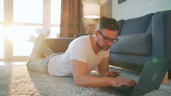 Man with Glasses Is Lying on the Floor, Working on a Laptop. Concept of Remote Work