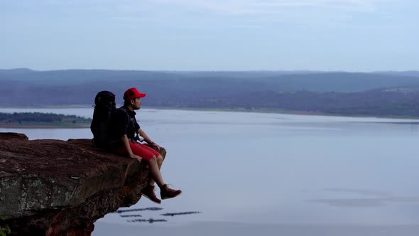 man traveler with backpack sitting on the edge of cliff and swinging Legs