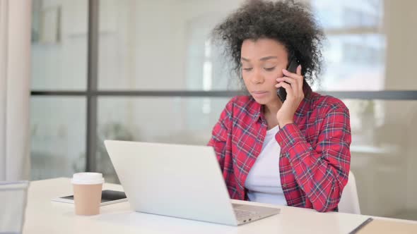 Angry African Woman Talking on Phone While Using Laptop