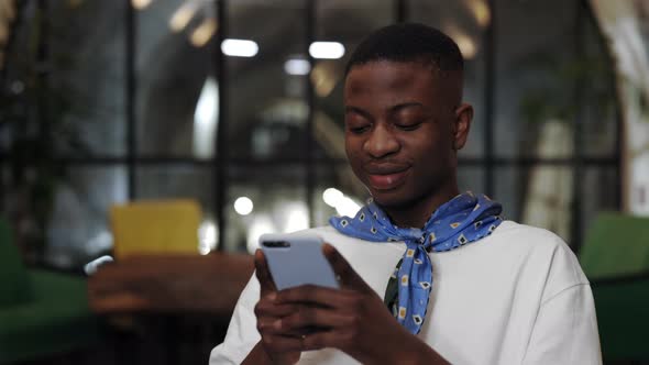 Crop View of Millennial Afro American Guy Using Smartphone and Laughing While Sitting in Cafe