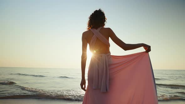 Woman Holds and Lets Go of Her Dress Against Sunset Sea Background