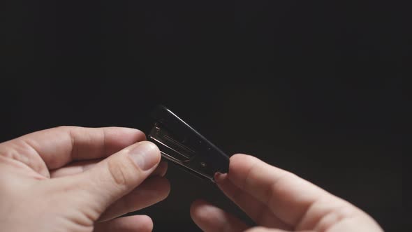 Man's Hand Holds a Stapler on a Dark Background. Close Up