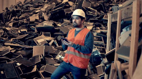 Dumpsite Worker with a Smartphone is Standing Near a Pile of Rubbish