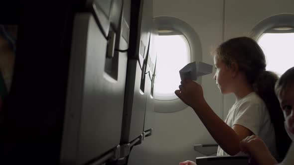 Child Sitting By Aircraft Window and Playing with Little Paper Plane During Flight on Airplane