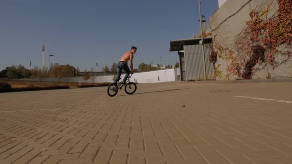 Athletic Muscular Young Man Without a T-shirt Rides a Stunt Bike in a Park.