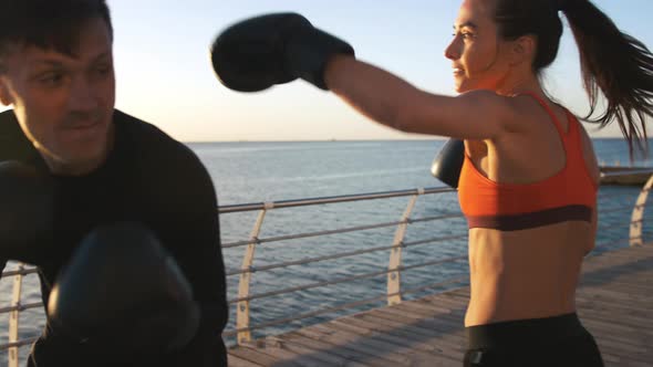 Young Lady in Boxing Gloves and Sport Clothes is Boxing with Her Skillful Trainer