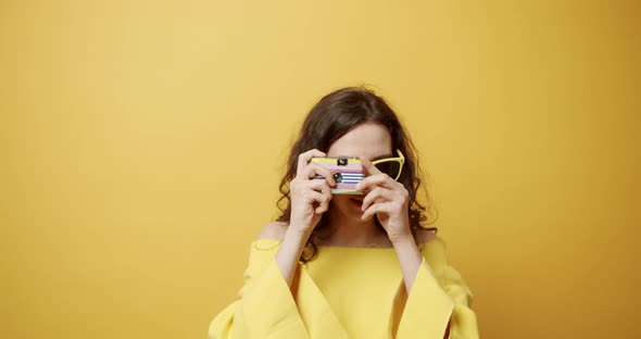 a Young Girl Smiles Takes a Picture with the Retro Camera on a Yellow Background