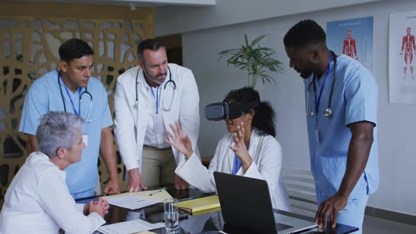 Asian female doctor at table using vr headset with a diverse group of colleagues gathered around her