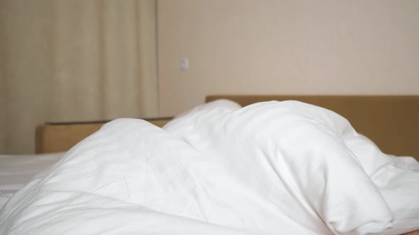 Cheerful Woman Rejoices and Plays with White Blanket on Bed