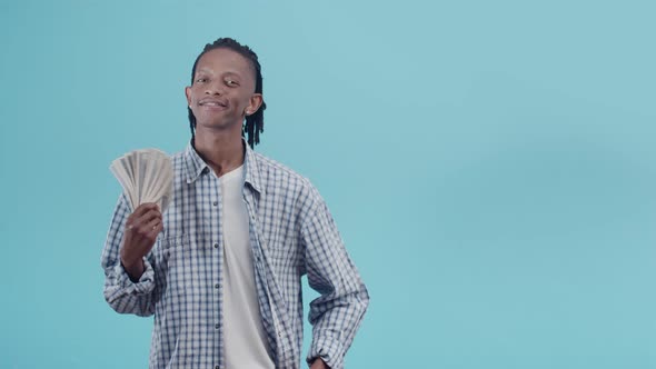 Black man with dreadlocks waves a bundle of dollar bills holding a fan in hand and staring