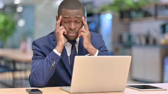 Stressed African Businessman with Laptop Having Headache in Office 