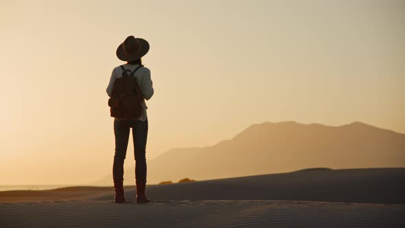 Young traveler with a backpack looking at the mountains at sunset