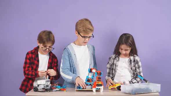 Smart Caucasian Kids Play and Assemble Futuristic Toys Isolated in Studio with Purple Background