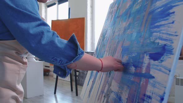 A Chubby Woman Paint Artist Drawing an Abstract Blue Painting with a Palette Knife