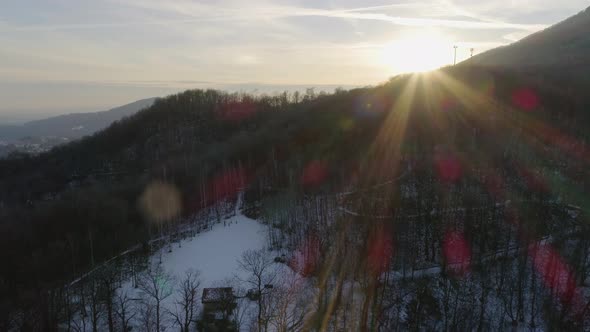 Aerial Drone Flight Over Snowy Forest Woods at Sunset with People Walking