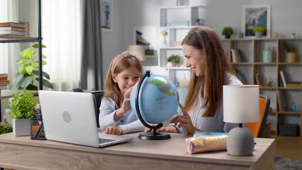 Mom and Daughter Study Geography with a Globe at Home