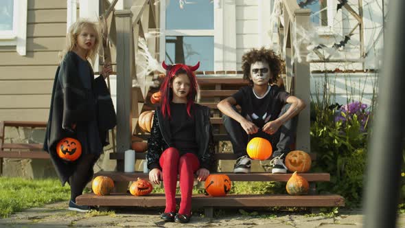 Three Kids in Halloween Costumes Sitting on Porch