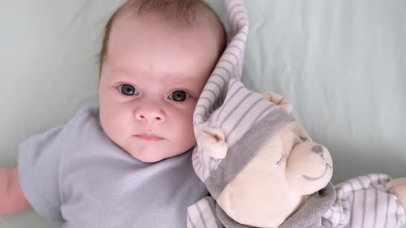 Newborn Baby Boy 3 Months Old Lies in Crib Nursery with Blue Clothes on His Back with Teddy Bear