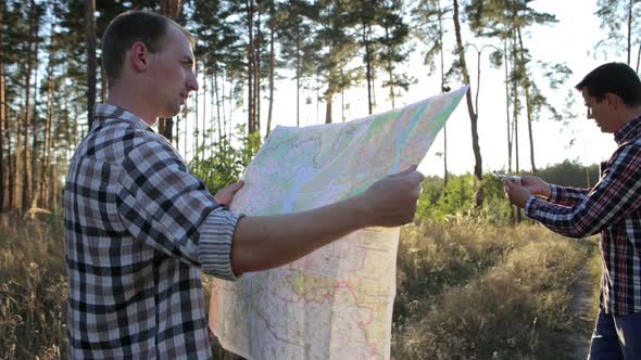 Travelers with a map and a compass in their hands are looking for their way. Terrain orientation.