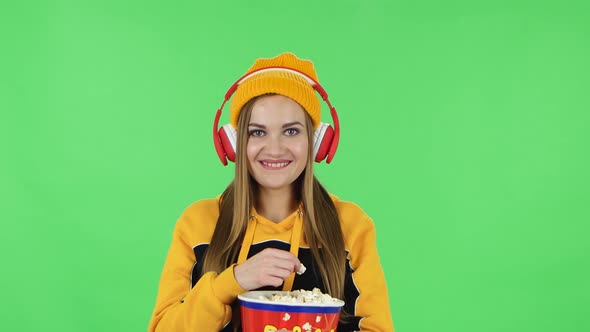 Portrait of Modern Girl in Big Red Headphones Is Watching a Funny Movie and Eating Popcorn. Green