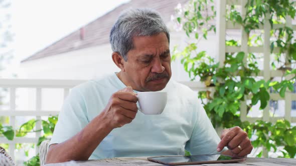 Senior mixed race man having coffee using tablet in garden