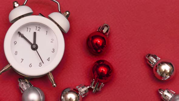 White Small Alarm Clock with Christmas Balls on a Red Background Closeup