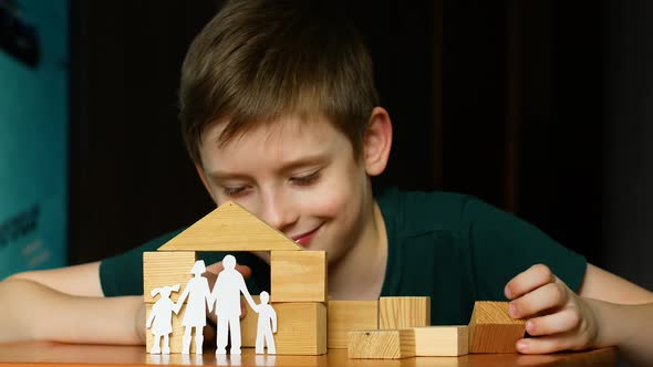 A happy cheerful Caucasian boy 7 years old plays with a family cut out of paper and builds a house f