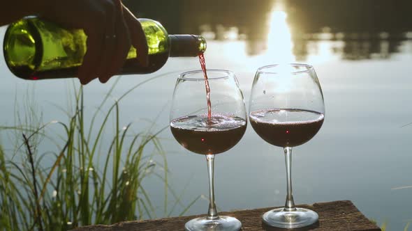 Slowmotion Red Wine Pouring From Bottle to Two Clear Glass on the Background of the Water Surface of