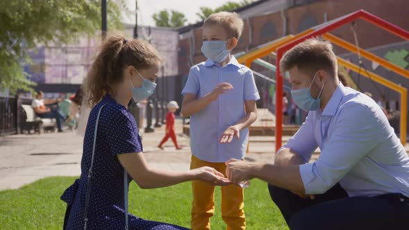 Young Family in Safety Mask Using Antiseptic Gel to Disinfect Hands Outdoors