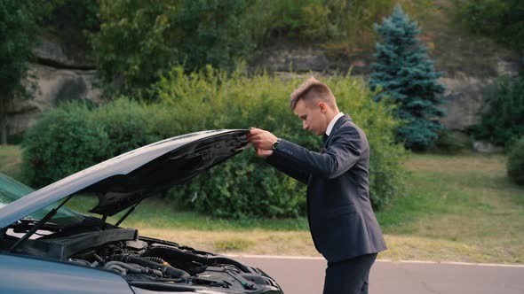 Side View of a Young Businessman Repairing Broken Car in Outdoor