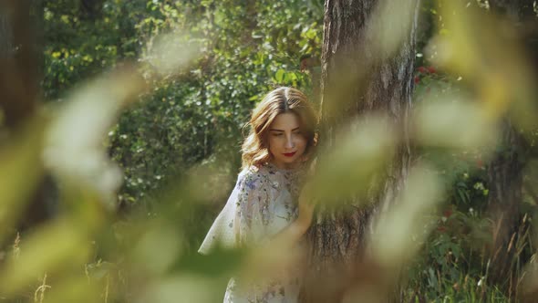 Portrait of Beautiful Young Caucasian Woman with Red Lips Posing in the Forest Near Tree Bark