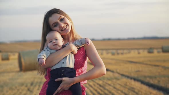 Happy Portrait of Smiling Mother with Her Baby Son in Hands Having Joy in Field