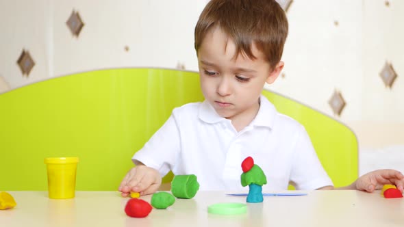 A Child Sitting at the Table, Plays in Colorful Sculptures of Plasticine or Dough for Games