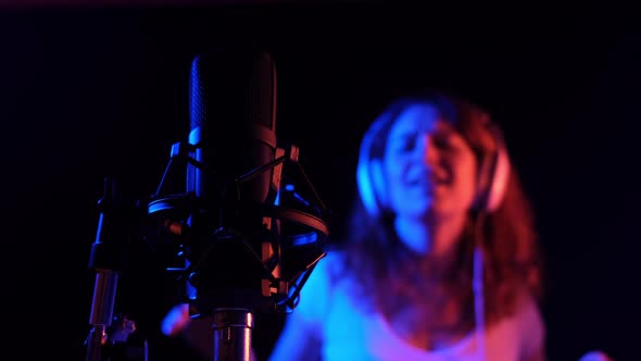 Caucasian Woman in Headphones Singing Into a Microphone in Neon Light on a Black Background