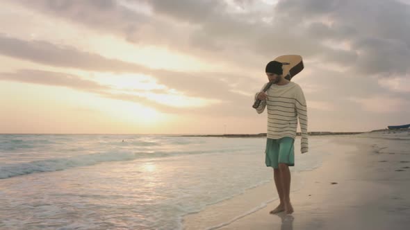 Front View of Young Beautiful Man with Guitar Walk Along on Ocean Beach Seaside at Sunrise or Sunset