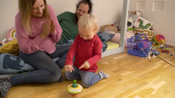 Father and mother showing spinning toy to Infant son at children room.