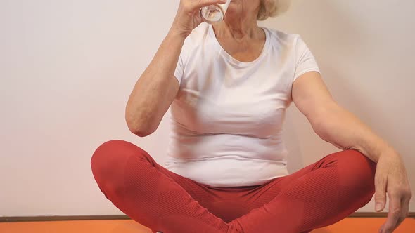 Positive Woman of Retirement Age Drinks Water After Yoga and Fitness Classes Sitting at Home on a