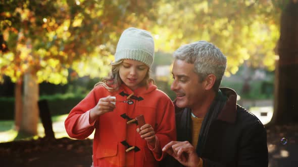 Girl blowing bubbles held by dad outdoors