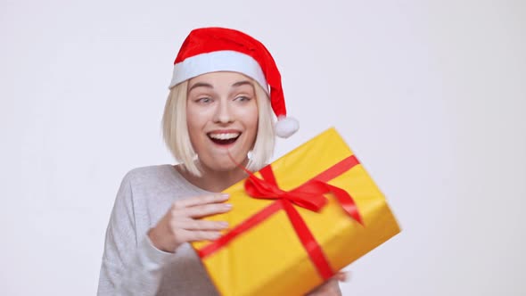 Young Beautiful Blonde Girl in Christmas Hat Suddenly Getting Gift Box White Background