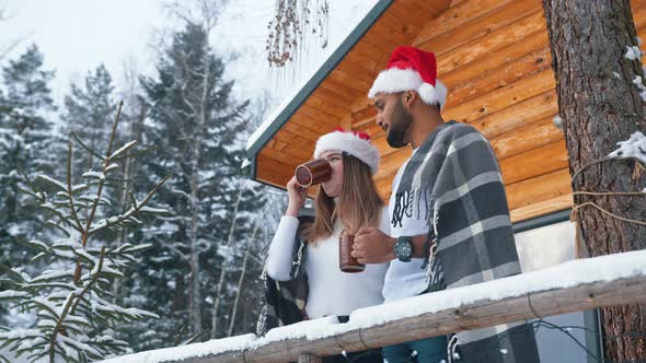 Young Couple in Front of the House is Drinking and Watching with Santa's Hat in the Distance