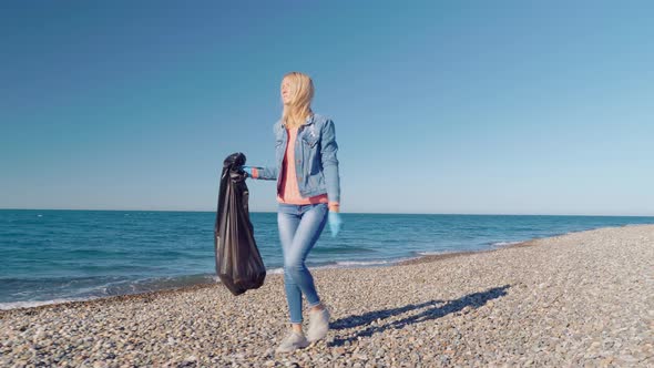 a female volunteer collects garbage in a black garbage bag.