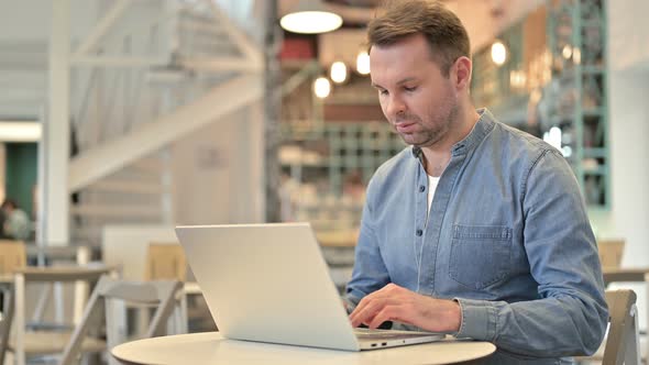 Casual Man with Laptop Smiling at Camera in Cafe 