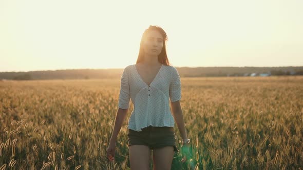 Pensive Girl Is Walking Alone in Sunset Time on Golden Fields with Wheat