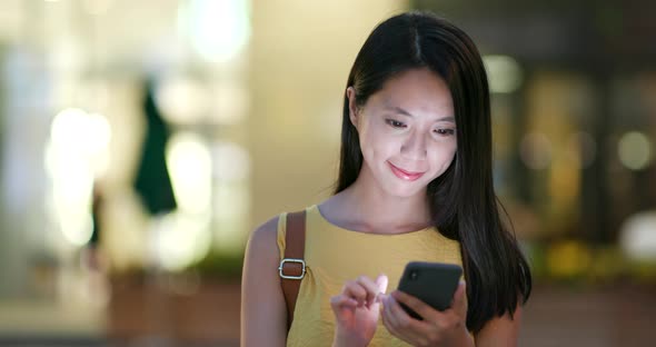 Woman sending audio message on cellphone in city of Shenzhen at night